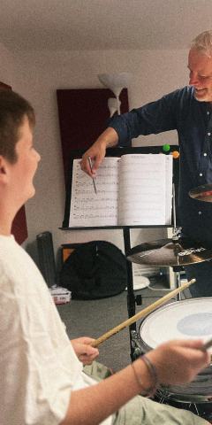 Schlagzeuglehrer erklärt einem Schüler am Drumset die Noten