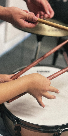 Hände von Lehrer und Kind mit Drumsticks auf einer Snare Drum